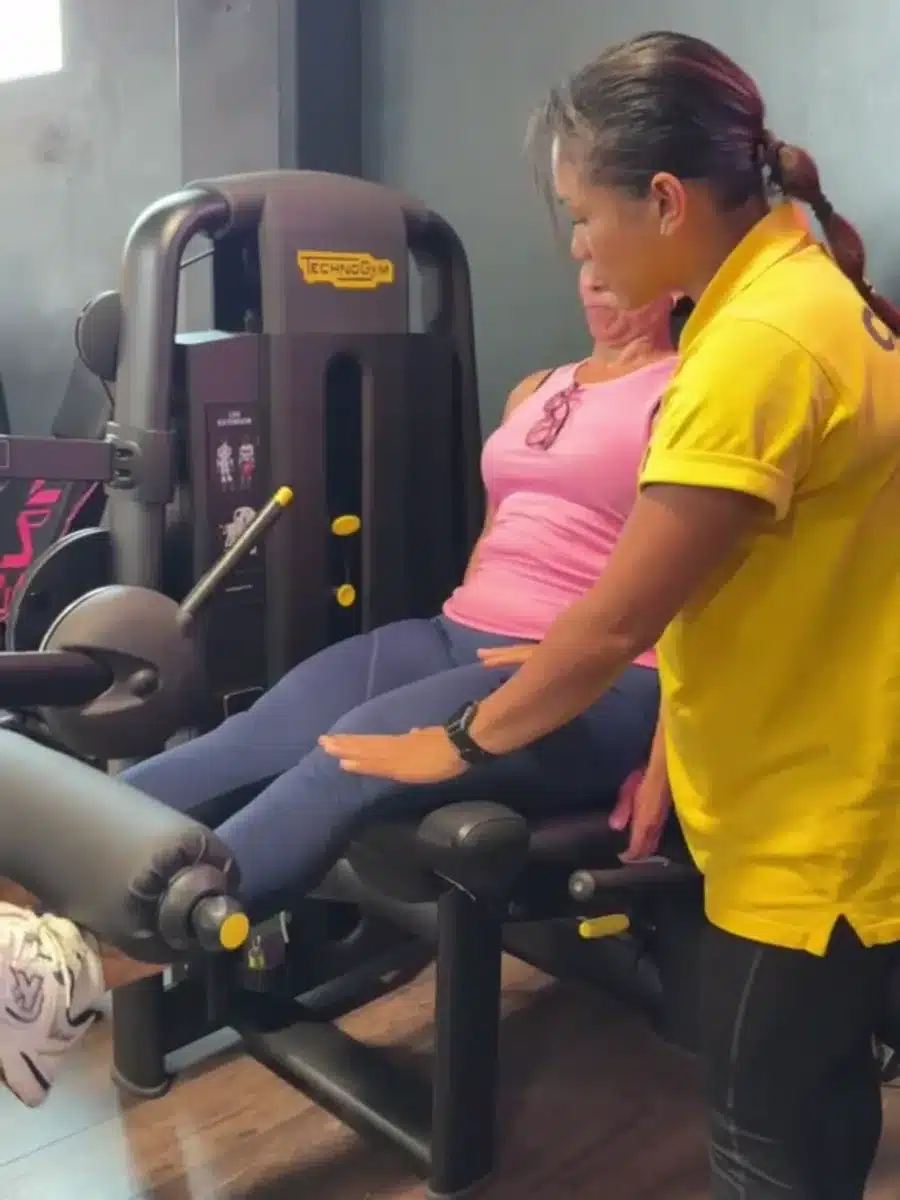 Coach de BodyLine corrigiendo la técnica de una clienta en la máquina de extensión de piernas
